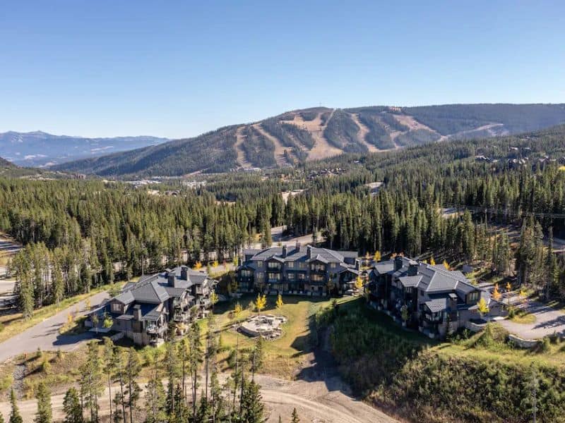 An aerial view of a Big Sky resort in summer with mountains in the background.