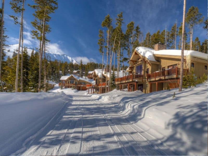 Winter view of snow-covered roads flanked by luxury cabins in Big Sky, illustrating the beauty of ski in ski out lodging in the area.