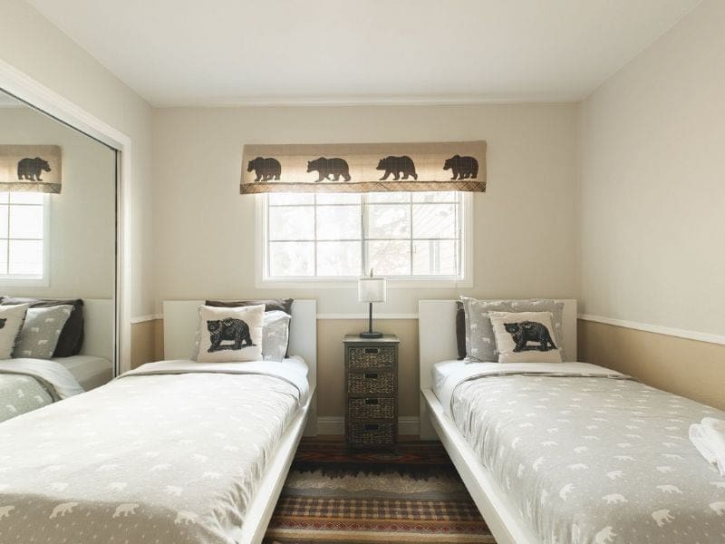 Twin beds with bear-patterned bedding and forest-themed decor in a Big Bear winter cabin rental on Vrbo.