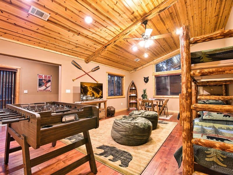 Cozy game room in a Big Bear winter cabin rental, showcasing a foosball table, comfortable seating, and mountain-themed decor under a pine wood ceiling.