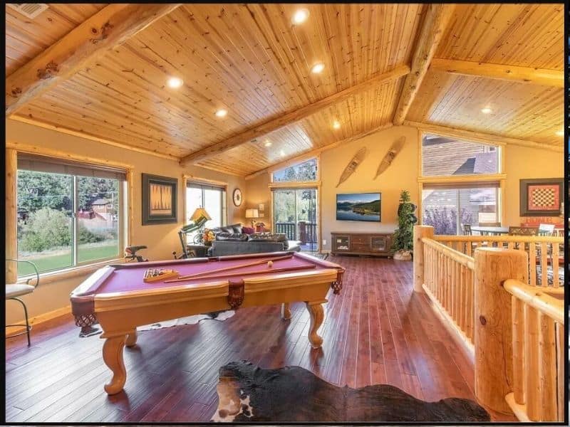 Expansive game room with a billiards table, leather seating, and a panoramic view of the outdoors. One of the best cabin rentals near Bear Mountain in Big Bear.
