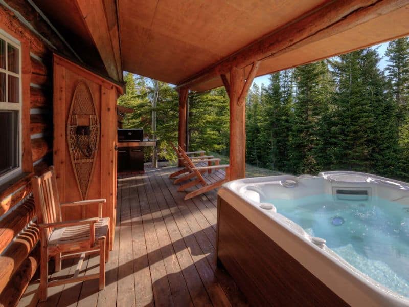 A Big Sky MT rental featuring a hot tub on the deck of a log cabin.