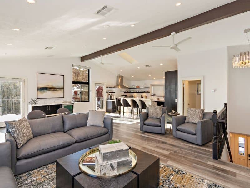 Contemporary open-plan living space with chic gray sofas and a central fireplace, offering an easy transition to a state-of-the-art kitchen in a Big Bear winter cabin rental.
