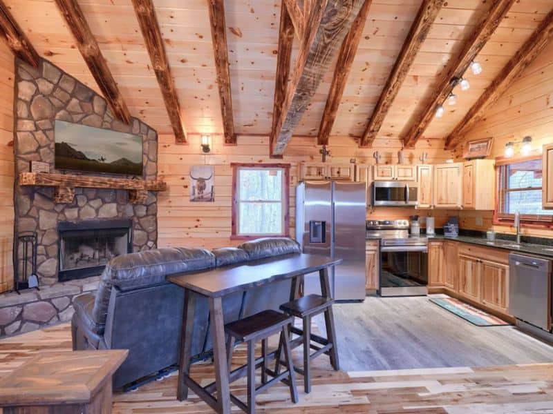 Open living area and kitchen in Hocking Hills wood cabin rental with a stone wood-burning fireplace and vaulted ceilings.