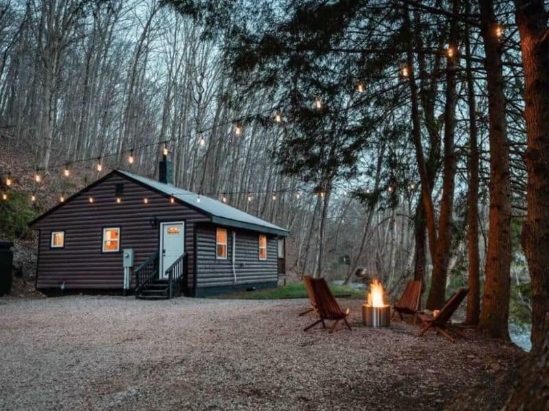 Evening view of a Hocking Hills cabin for 2 with outdoor string lights and a fire pit, set in a wooded area.
