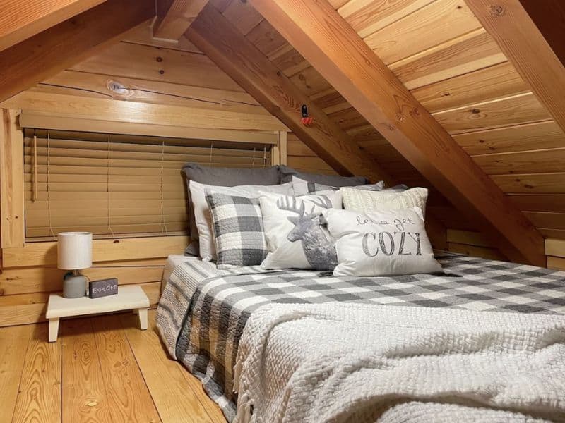Queen loft bed with lots of pillows and a checkered duvet in a tiny cabin rental in Hocking Hills OH.