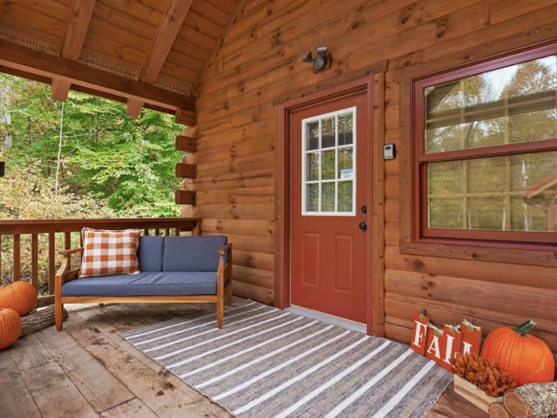 Entrance to cozy log cabin with orange door and outdoor couch on the stoop. Part of a guide to the best Hocking Hills Cabins for 2.