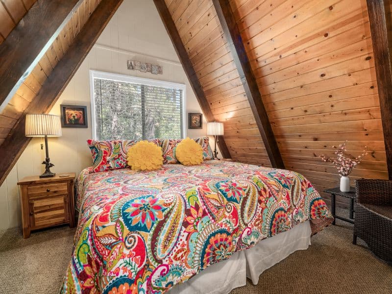 Cozy attic bedroom with a vibrant, patterned comforter and wooden interior in a Big Bear winter cabin rental on Vrbo.