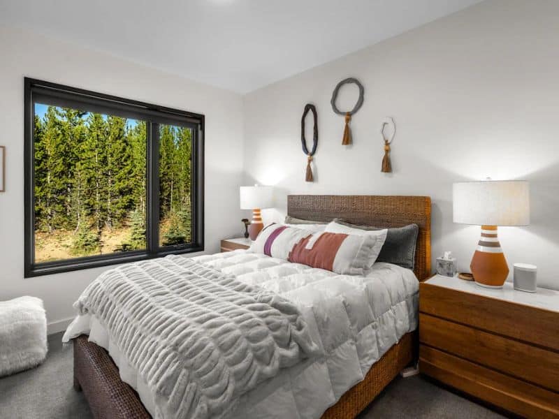 A bedroom with a window view of dense pines, part of a well-appointed rental, offering a peaceful retreat after a day on the Big Sky slopes.