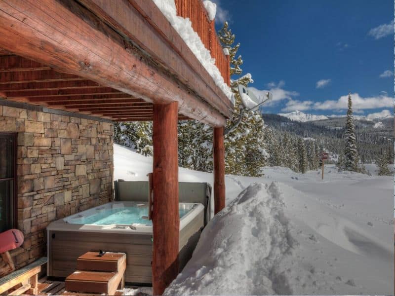 Hot tub on a snow-covered deck with mountain views at a ski in ski out rental in Big Sky, Montana.