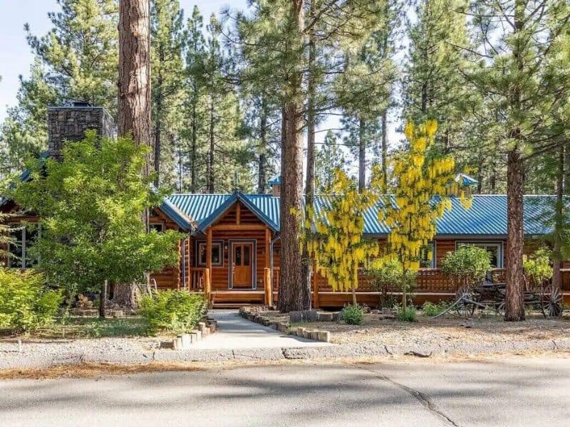 Exterior of a Big Bear log cabin rental surrounded by tall pines and clear skies, with a welcoming front porch.