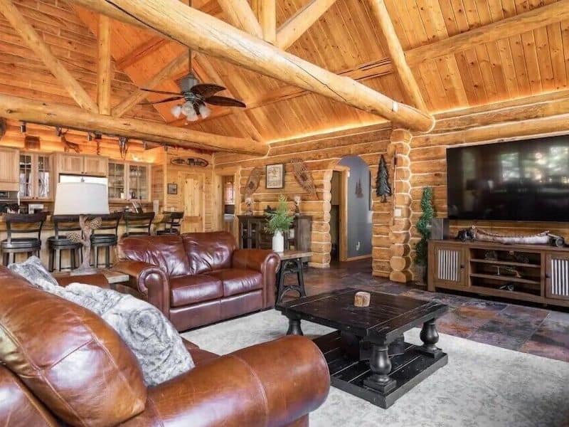 Rustic living room inside a cabin near Snow Summit in Big Bear, featuring leather sofas, a large coffee table, and log beam ceilings.