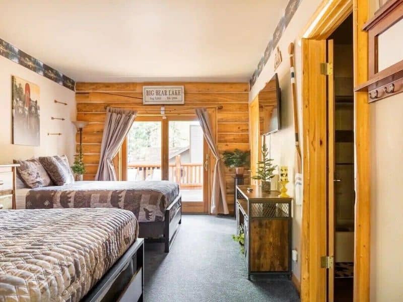 Twin queen bedroom with direct access to the deck in one of the best cabins near Snow Summit in Big Bear, decorated with mountain-themed bedding and wooden furnishings.