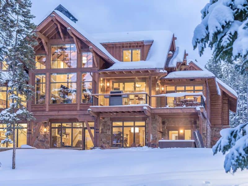 Twilight view of a multi-story ski in ski out Big Sky MT rental with large windows and a snow-covered exterior.