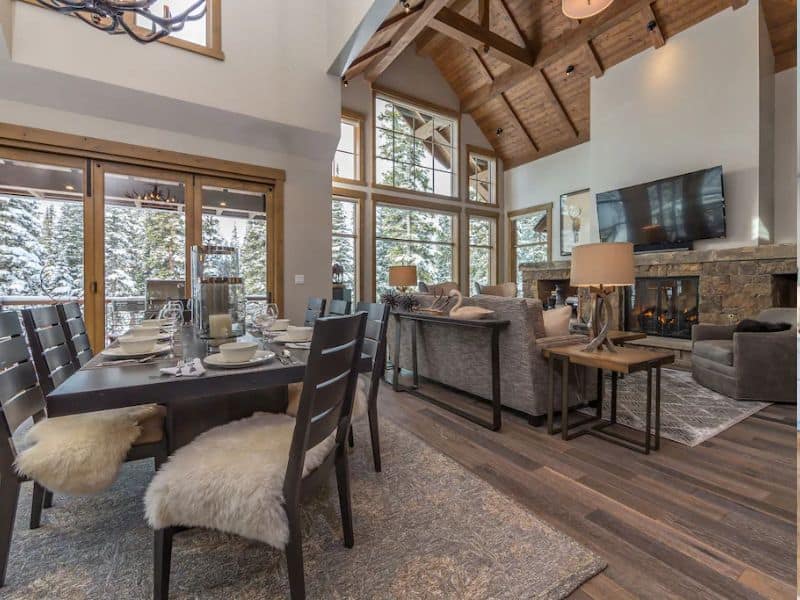 Open-concept dining and living space with large windows and a fireplace in a Big Sky vacation rental.