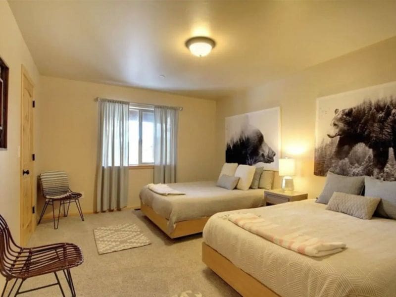 Warmly lit bedroom featuring two queen beds with plush bedding, adorned by large bear artwork, part of a guide to the best cabins near Bear Mountain in Big Bear.