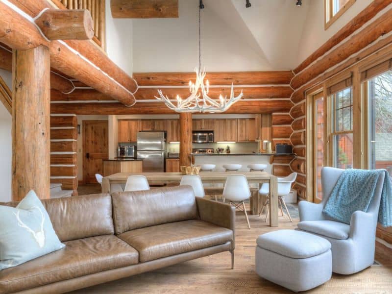 Spacious living area with exposed log beams and a modern kitchen in the background in a ski in ski out rental in Big Sky, MT.