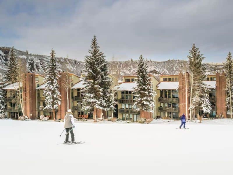 A group of people skiing in front of an apartment complex in Snowmass, Aspen.
