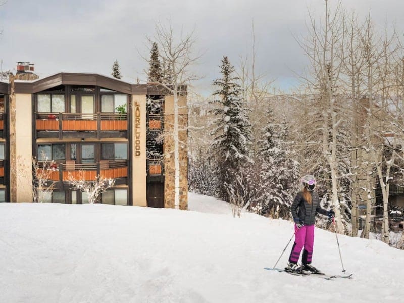 A skier in Snowmass Aspen on a snowy slope with a ski in ski out condo complex in the background.