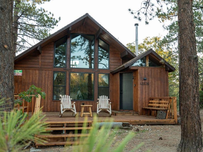 Exterior view of a cabin rental near Bear Mountain in Big Bear, showcasing its high A-frame structure, expansive windows, and a front deck with chairs.