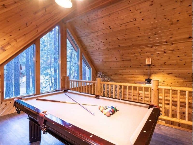 Loft game room with a pool table and large windows offering forest views, a perfect entertainment space in a Big Bear cabin rental.
