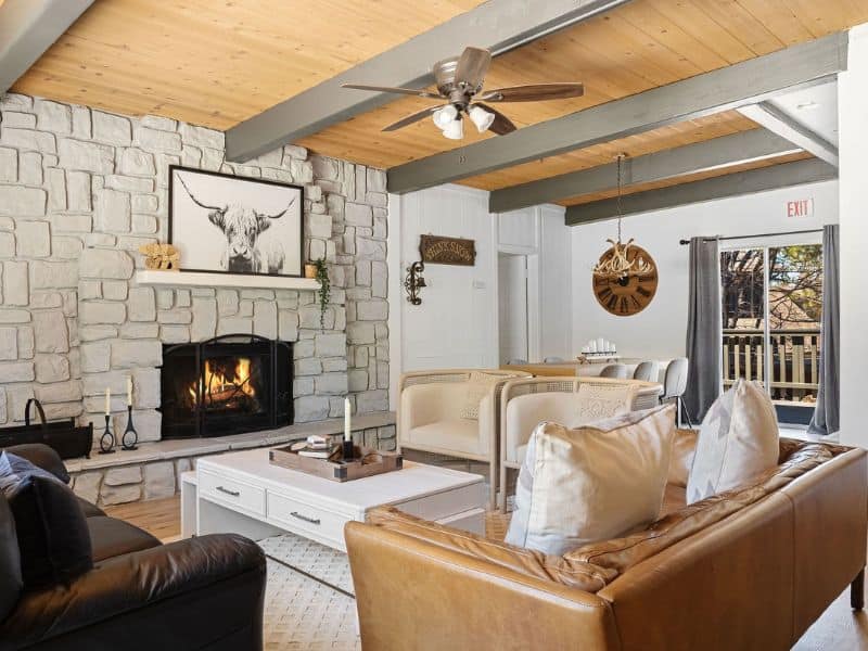 Living room with a white stone fireplace and wooden beams, a warm and inviting space in a Big Bear winter cabin rental.