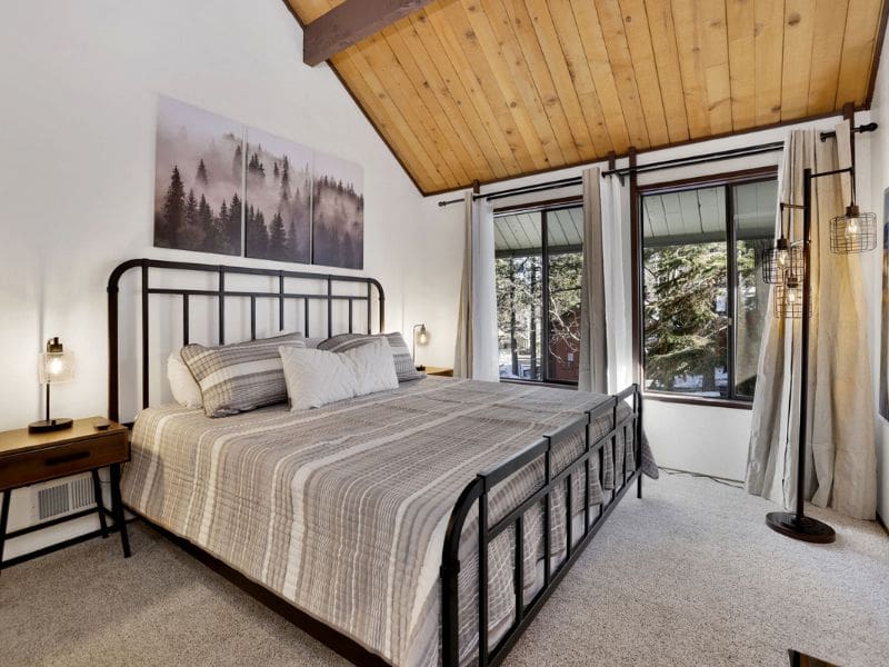 Cozy bedroom with a king-sized bed in a cabin near Snow Summit, featuring large windows with forest views.