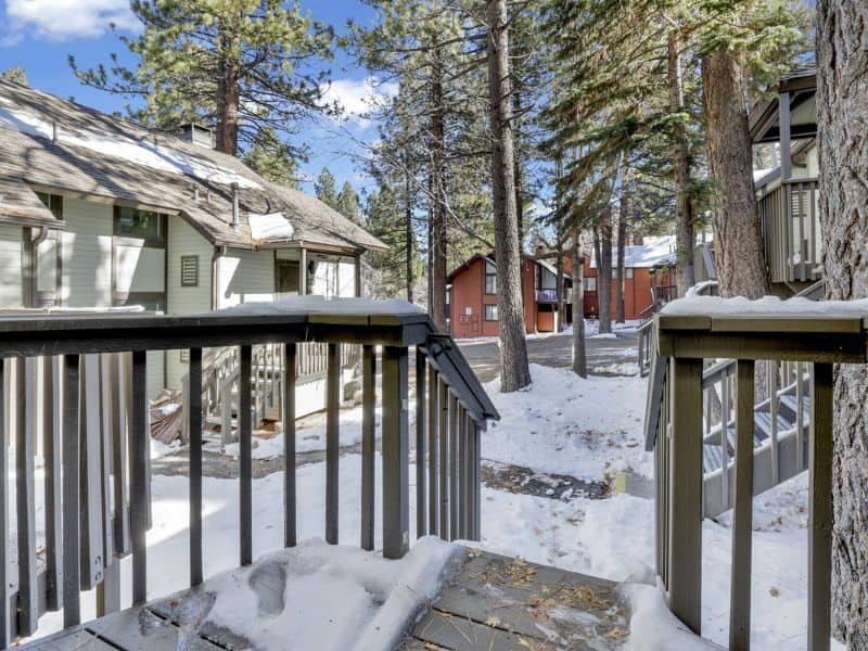 View from a Big Bear winter cabin's deck with snowy grounds and surrounding pine trees, showcasing nearby cabins.
