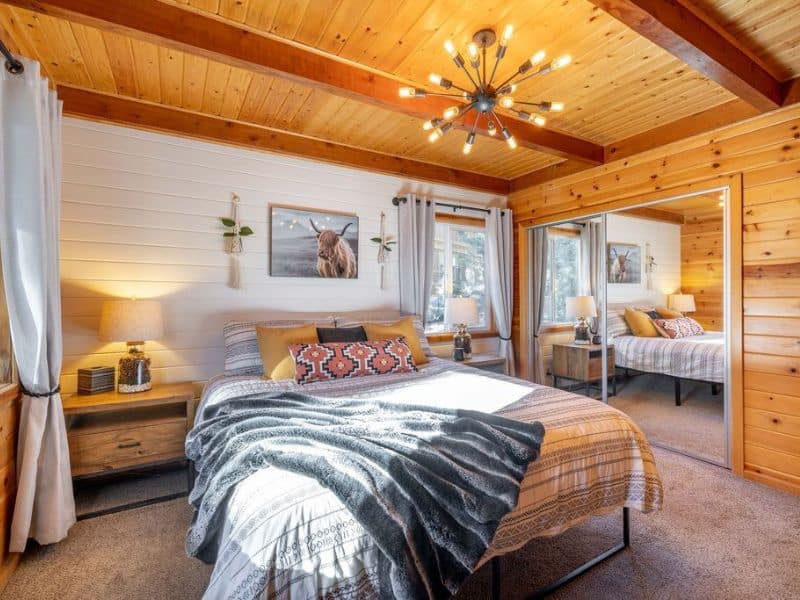 Warmly lit bedroom with rustic decor and a large bed in one of the best cabin rentals near Bear Mountain in Big Bear, showcasing wood-paneled walls and a plush comforter.