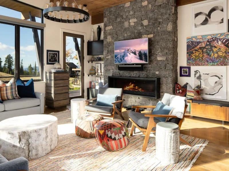 Modern living room with a stone fireplace and chic decor in a Big Sky Montana Vrbo, with ample seating and natural light, offering a peaceful retreat post skiing adventures.