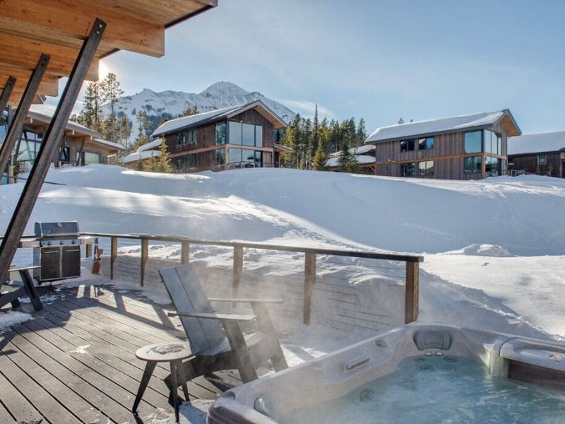 Steaming hot tub on the wooden deck of a ski in ski out Big Sky MT rental, with mountain views in the backdrop, perfect for relaxing after a day on the slopes.