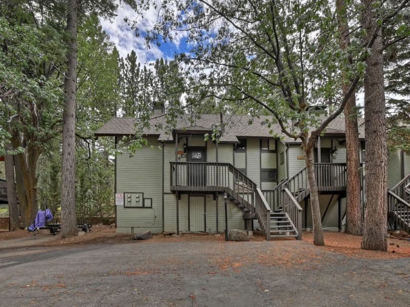 Exterior of a multi-story green condo complex surrounded by tall trees near Snow Summit in Big Bear CA.