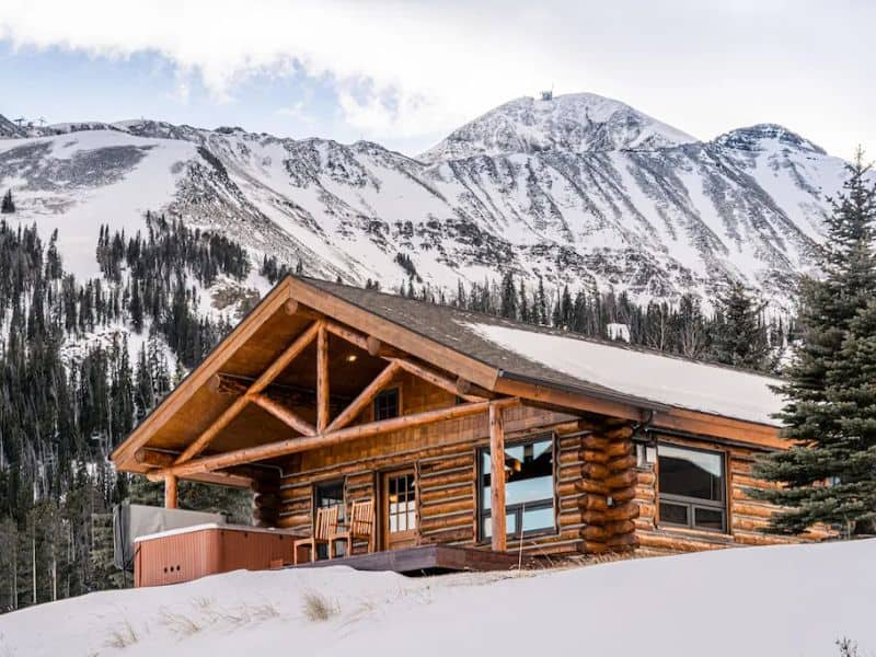 Rustic log cabin with a view of snow-covered mountains - a ski in ski out Big Sky MT rental.
