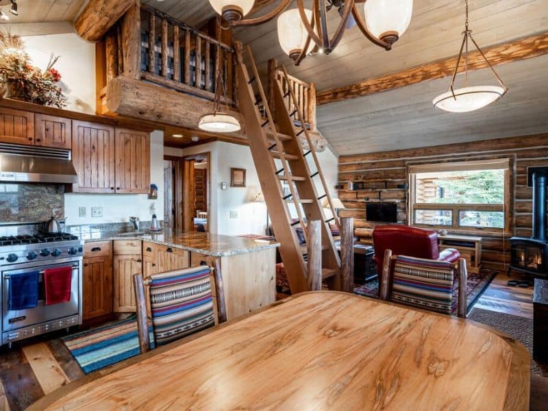 Cozy interior of a Big Sky rental cabin, featuring a warm kitchen with wooden finishes and a lofted sleeping area accessible by a rustic ladder.