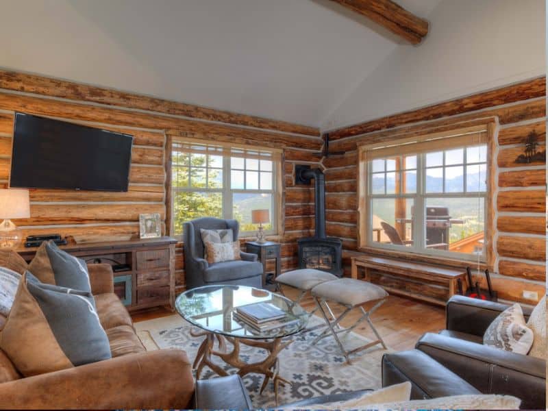 Cozy living area with plush seating and large windows in a Big Sky Montana rental cabin, offering stunning views and a warm fireplace.