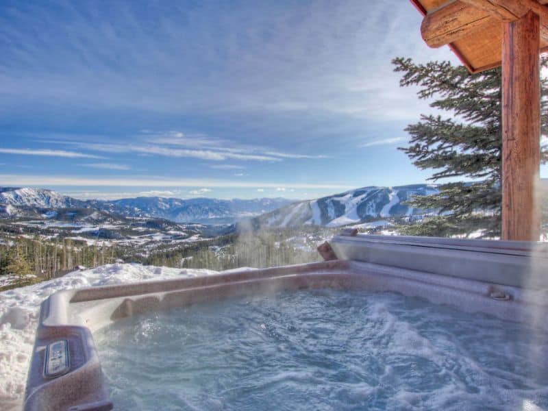 Hot tub on a cabin deck in Big Sky, Montana, with a sweeping view of snow-covered mountains, perfect for unwinding after skiing.