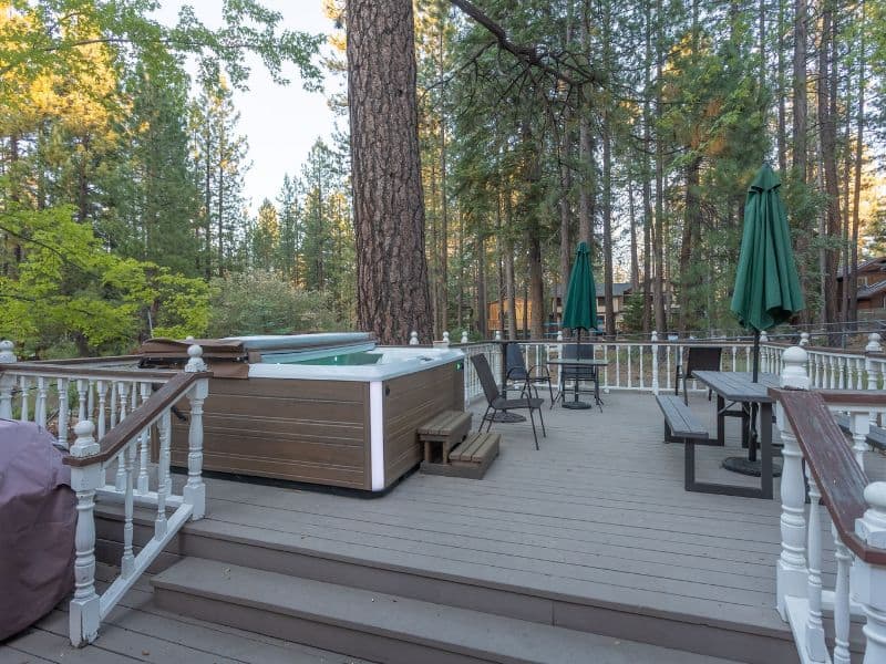 Outdoor deck of a Big Bear cabin with a hot tub and patio furniture surrounded by towering pines, ideal for après-ski relaxation.