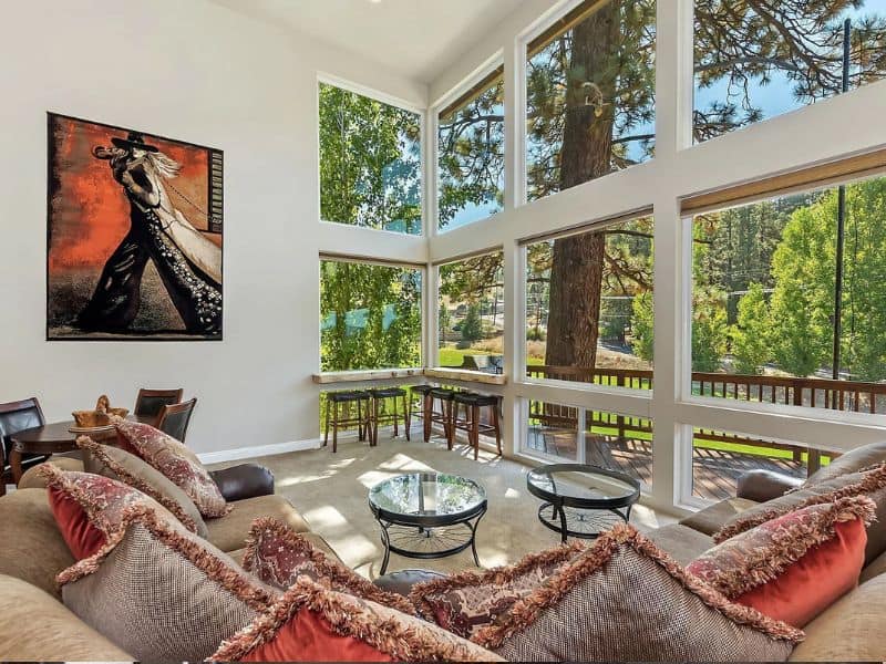 Spacious living area with large windows offering a view of pine trees, accented by a contemporary art piece and a comfortable sofa with throw pillows.