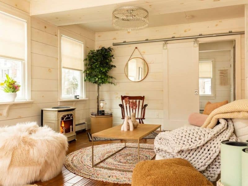 Bright and airy living room of a cozy Catskills cabin rental, with a plush sofa, eclectic rugs, and a wood-burning stove, offering a homely atmosphere.
