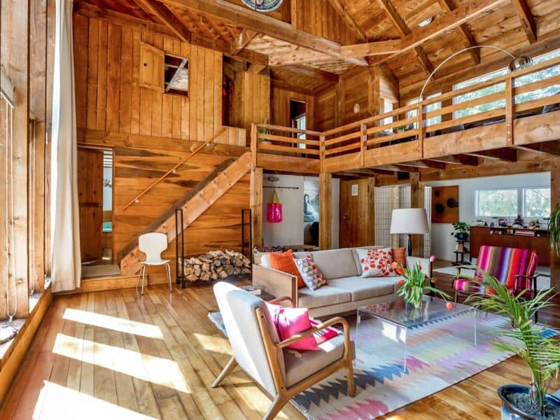 Spacious living room inside a cozy cabin in the Catskills, with a loft area, hardwood floors, and a mix of modern and rustic furnishings.
