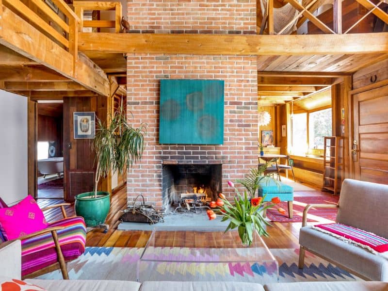 Warm and inviting living area with a brick fireplace, high ceilings, and eclectic decor in a winter Catskills cabin rental.