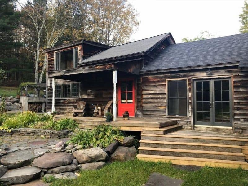 Exterior view of a cozy cabin in the Catskills, featuring a rustic wooden facade with a striking red door.