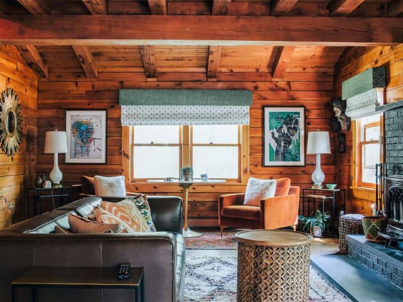 Interior of a cozy cabin in the Catskills featuring a warm living room with wooden walls, comfortable seating, and eclectic artwork.