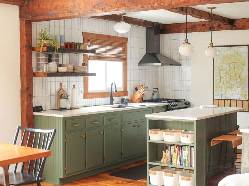 Stylish and functional kitchen in a Catskills cabin rental, with green cabinets, wooden open shelving, and vintage pendant lighting over a white countertop island.
