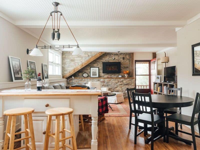 Bright and airy dining space in a Catskills cabin rental, with a stone accent wall, wooden ceiling beams, and a blend of modern and rustic decor.
