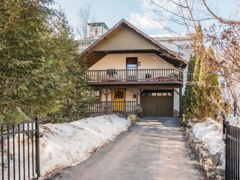 Exterior view of a winter Catskills cabin rental with a spacious balcony, a yellow door, and snow-covered surroundings.
