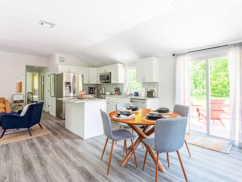 Open-plan kitchen and dining space in a cozy cabin in the Catskills, with a fully equipped kitchen, a round wooden dining table set for four, and natural light from large windows.