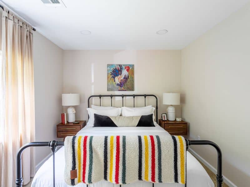 Comfortable bedroom in a cozy Catskills cabin rental with a metal frame bed, colorful striped blanket, and nightstands with lamps on either side.