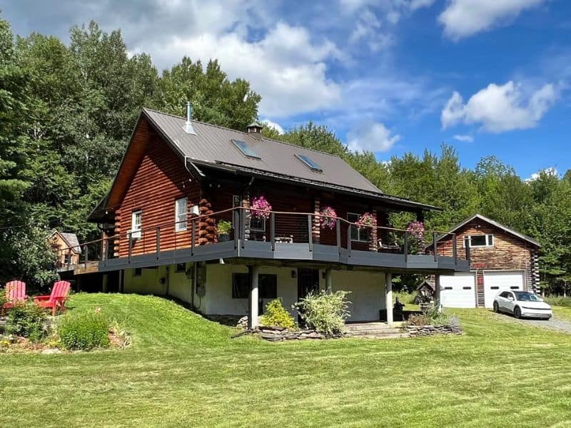 Exterior of a Catskills Vrbo log cabin rental with a large balcony and a green lawn.