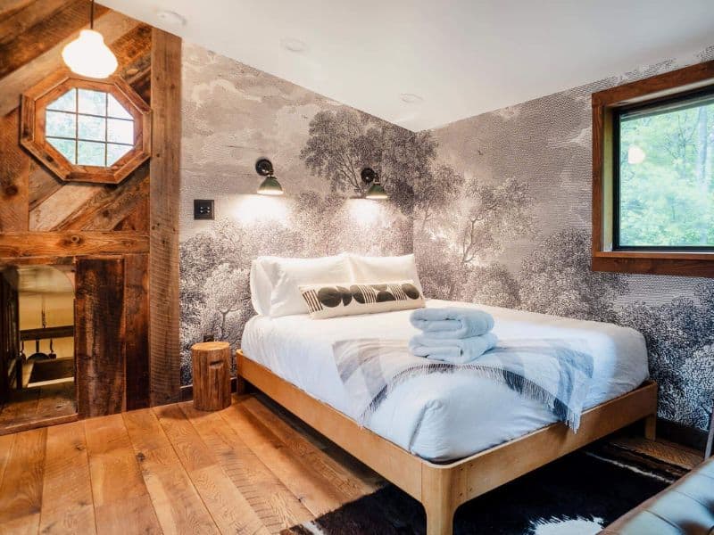 Bedroom in a cozy cabin in the Catskills with a forest wallpaper, wooden accents, and a comfy bed adorned with a striped throw and decorative pillows.